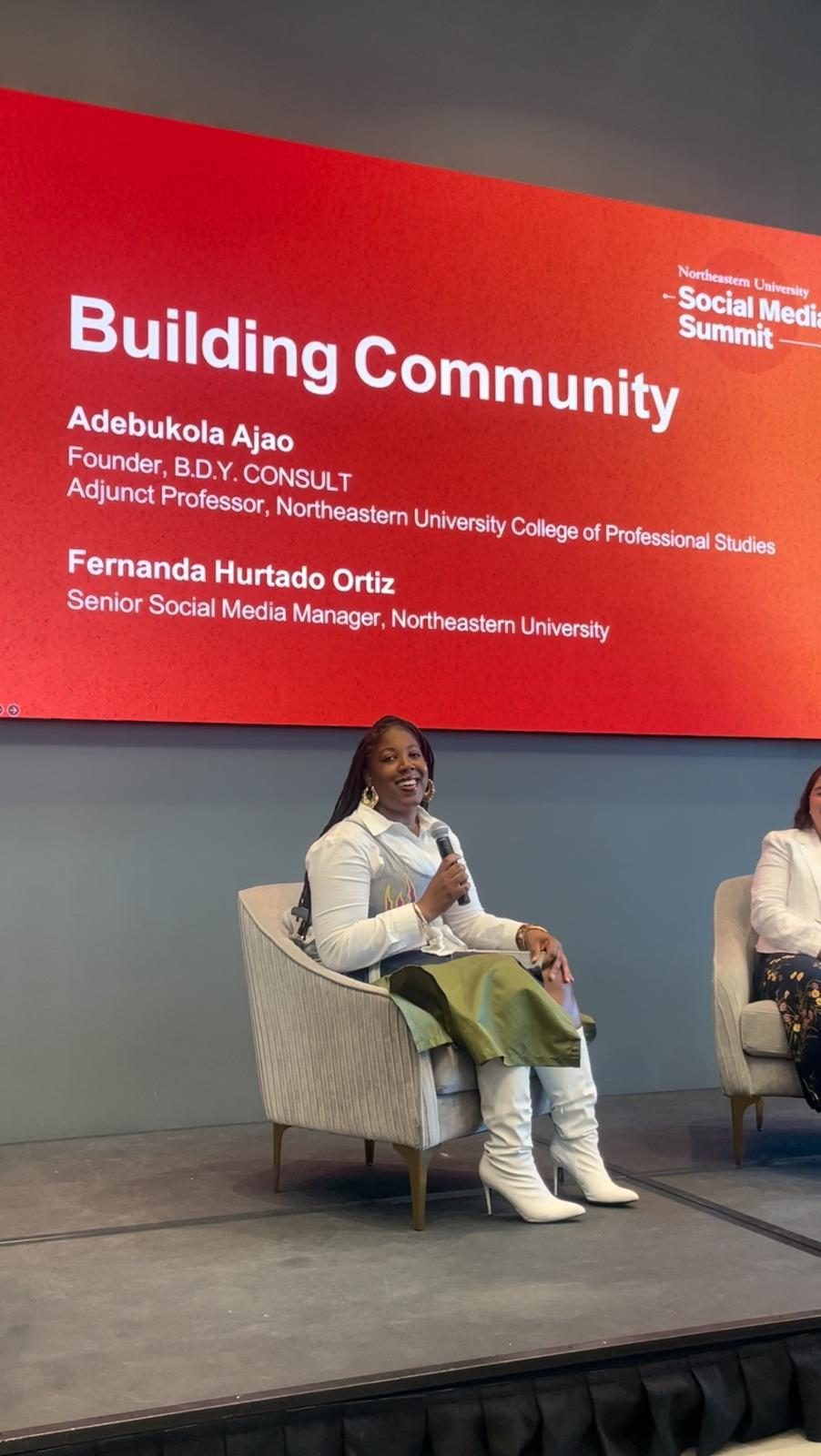 Adebukola Ajao speaking on a panel at the Northeastern University Social Media Summit, with a Building Community title slide behind her