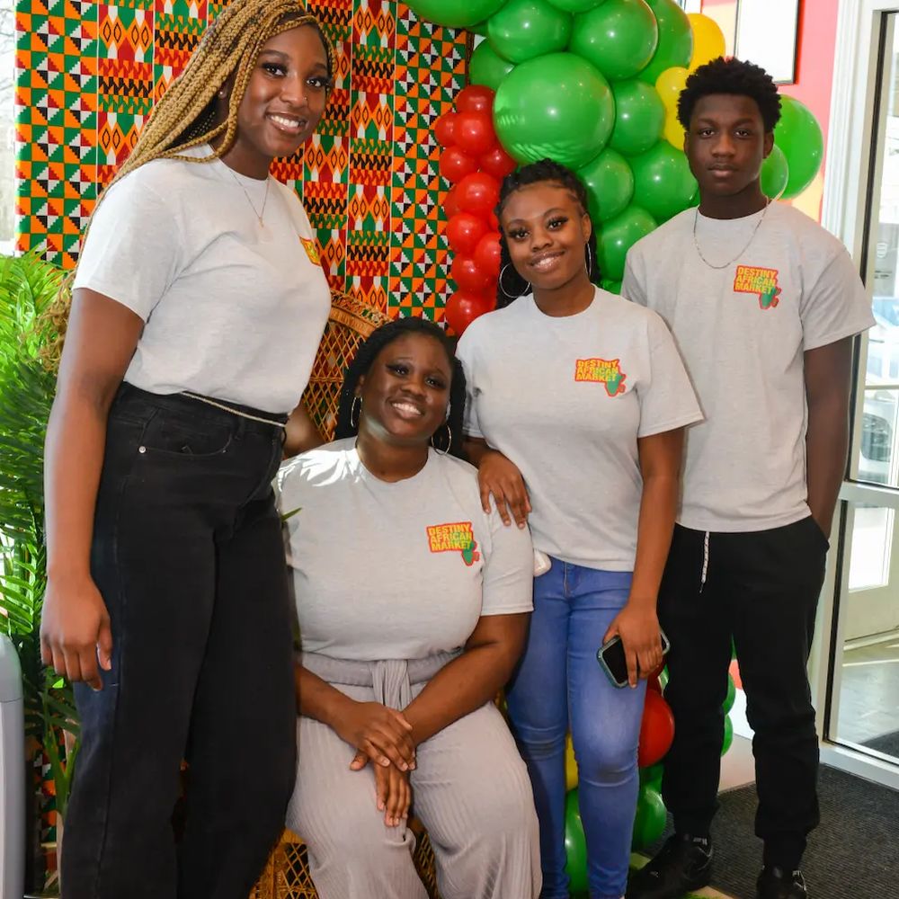 Four Destiny African Market team members in branded tees in front of a kente backdrop